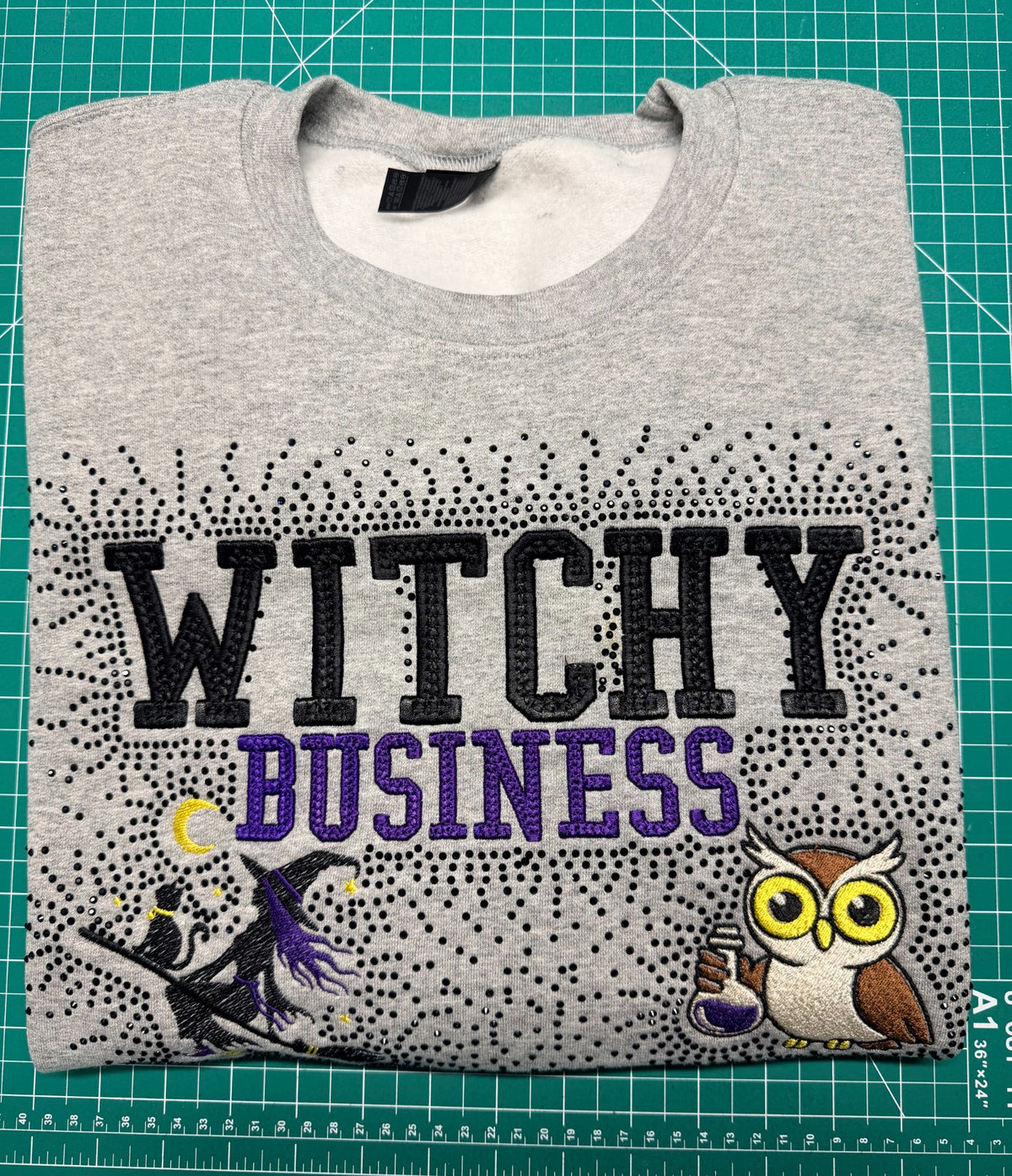 Close-up of gray Witchy Business embroidered sweatshirt with black rhinestones